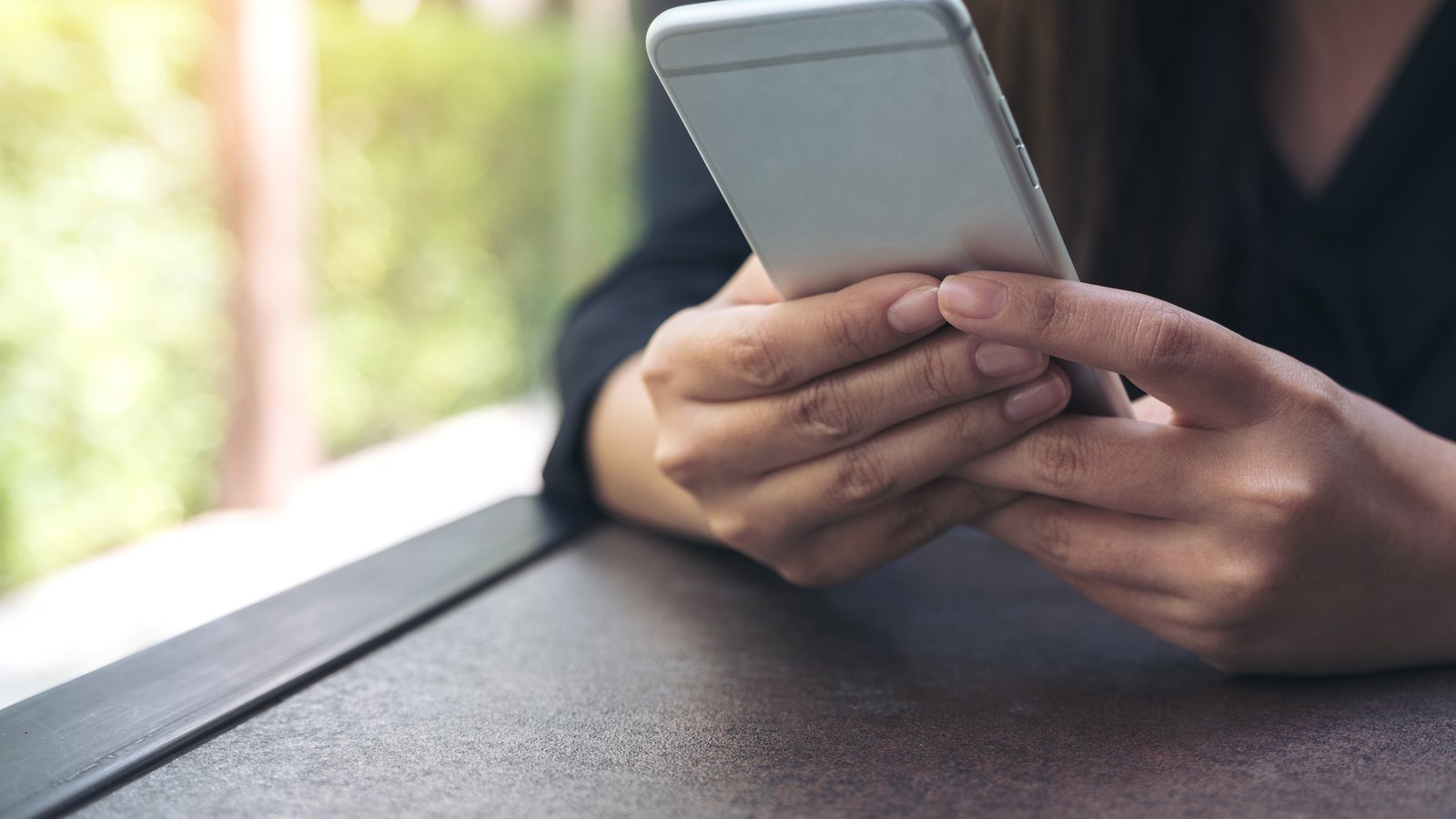 Mãos segurando um celular numa mesa escura